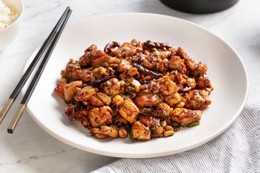 A plate of real-deal kung pao chicken with chopsticks on the side of the plate. 