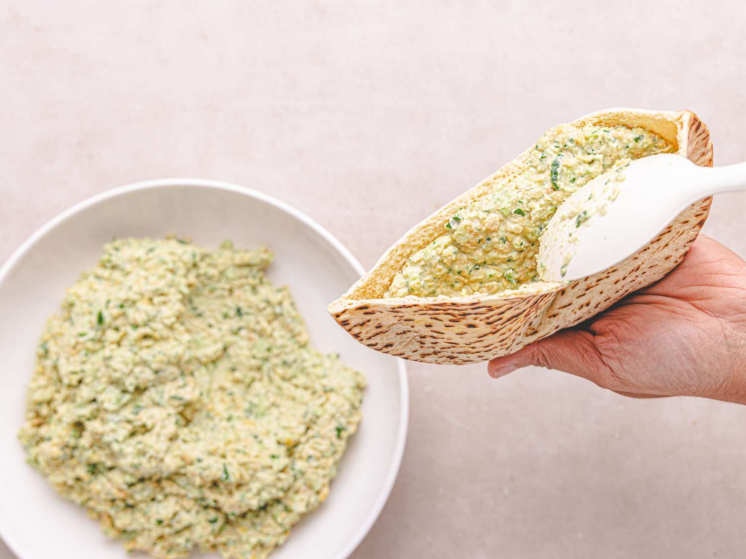 Hand filling pita bread with a chickpea salad mixture from a bowl