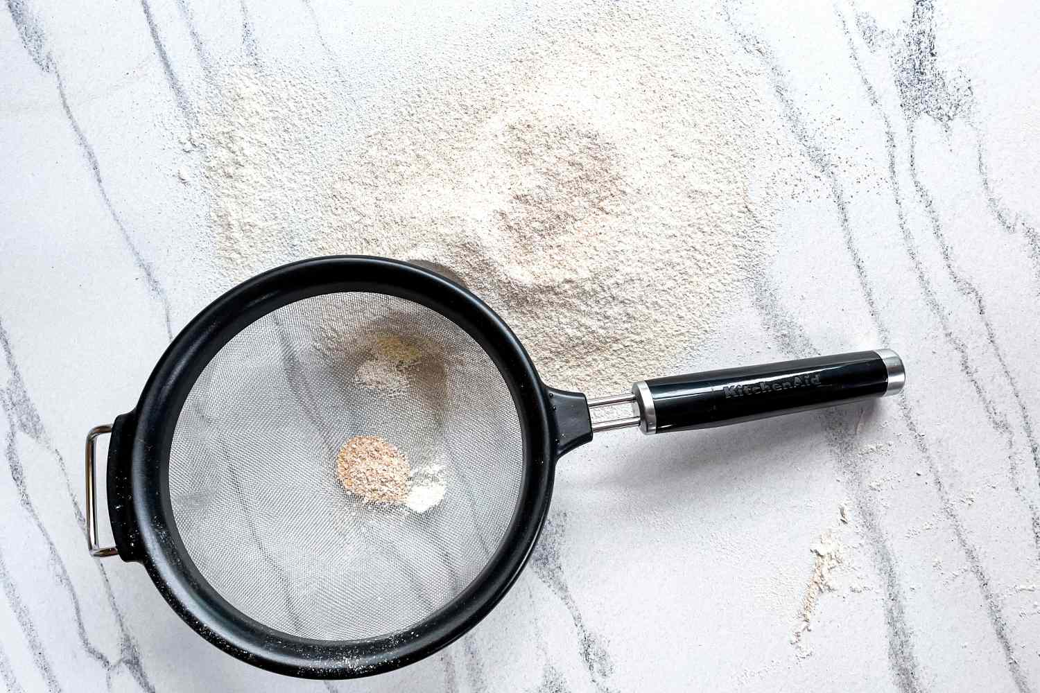 KitchenAid Classic Strainer with flour and a marble surface background showing baking preparation tools and materials