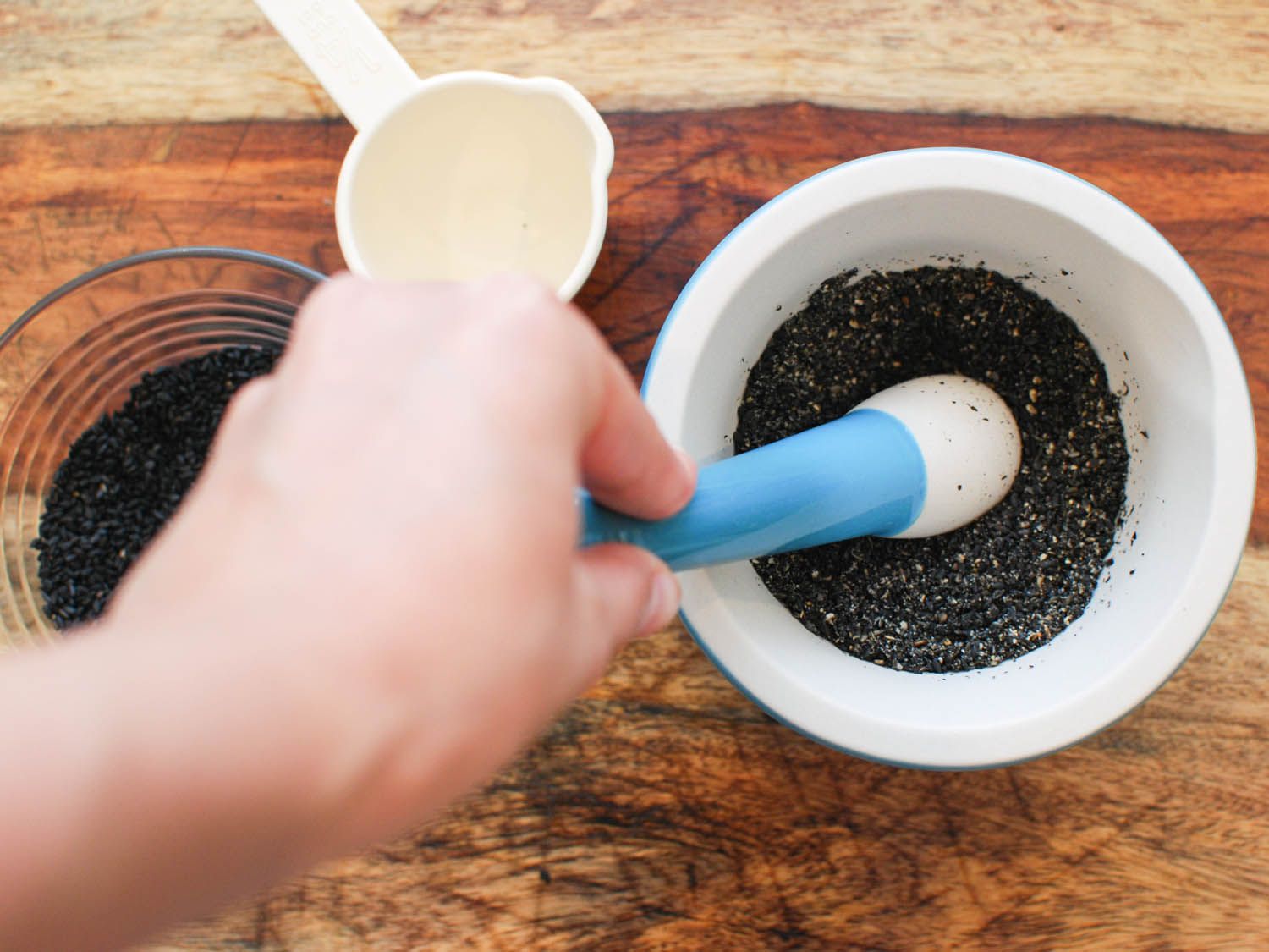 Black sesame seeds are crushed in a ceramic mortar and pestle.