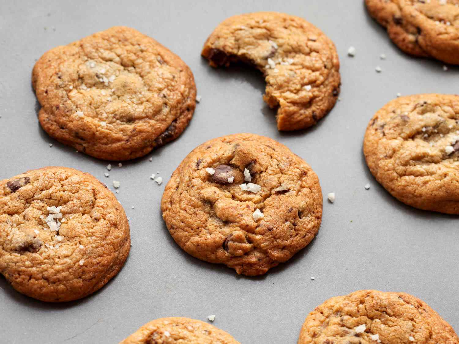 Chocolate chip cookies on a grey background with one cookie with a bite taken out.