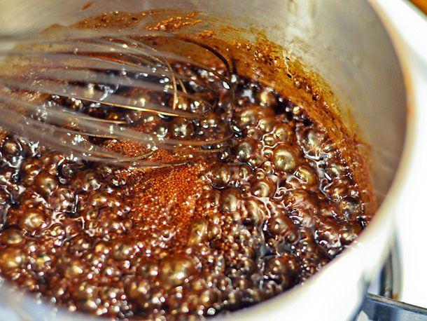 Ingredients for hoisin sauce are brought to a boil in a saucepan and stirred with a whisk.