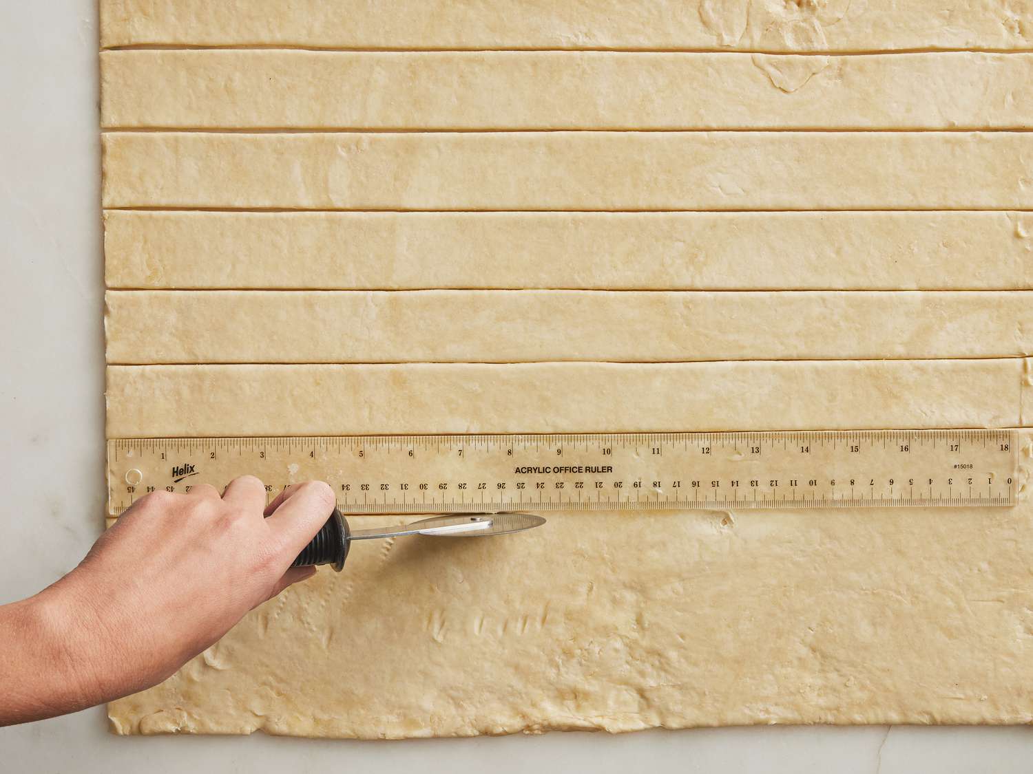 Using a measuring stick, dough is being cut into strips 