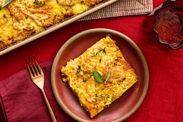 A serving of root vegetable gratin on a plate with a fork garnished with herbs and set on a red background