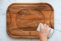 Person pouring water to clean Lipper International Acacia Cutting Board with Grid Grip