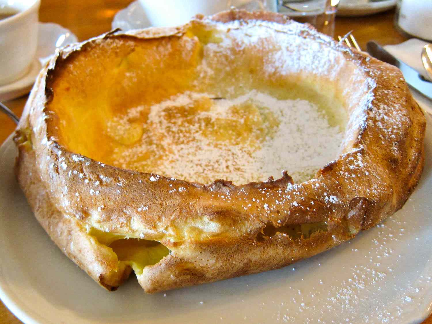 A large Dutch baby pancake on a platter sprinkled with powdered sugar. 