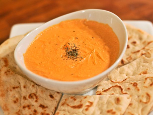 A small bowl of tyrokafteri (hot pepper and cheese dip), served on a platter with wedges of pita bread.