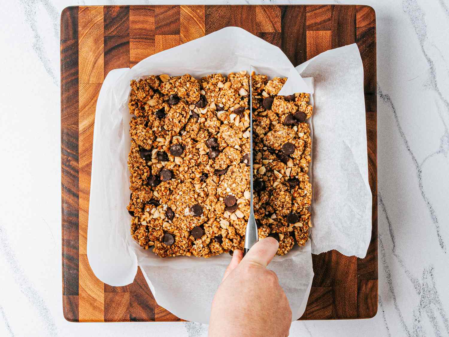 Baking tray with a large bar of granola being sliced using a knife on a cutting board