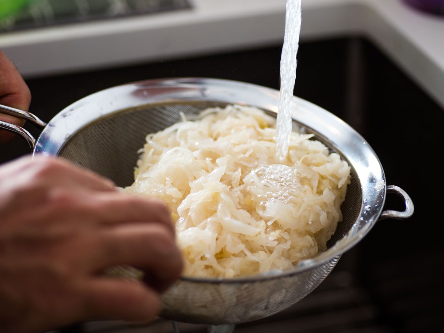 Sauerkraut being rinsed in a fine-mesh strainer for making choucroute garnie.