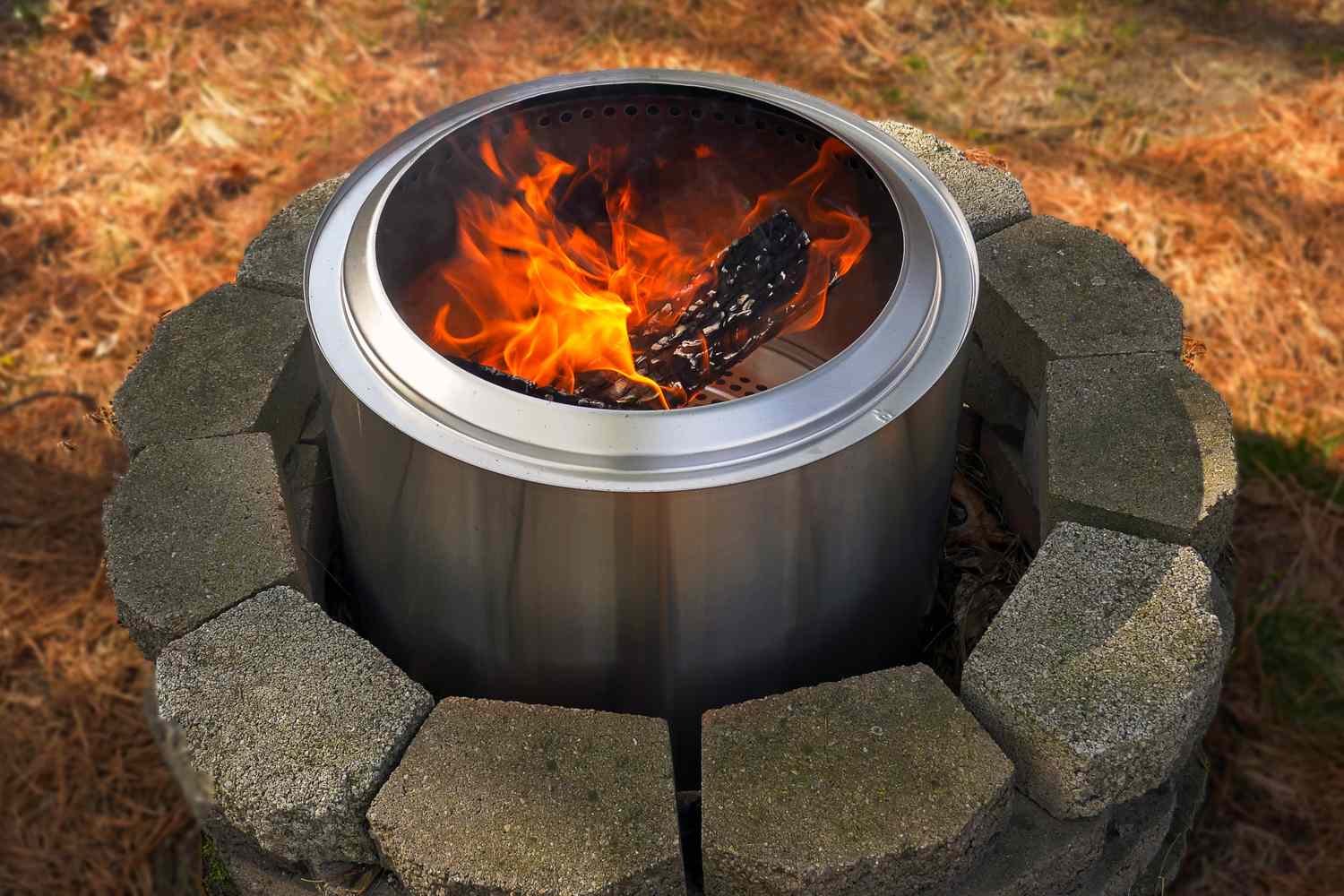 A metal fire pit burning logs, surrounded by a stone circle