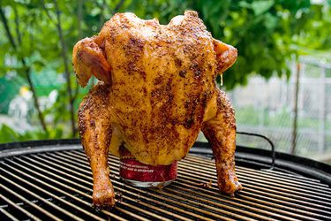 A whole chicken with a cola can in its cavity, roasting vertically over a grill. 
