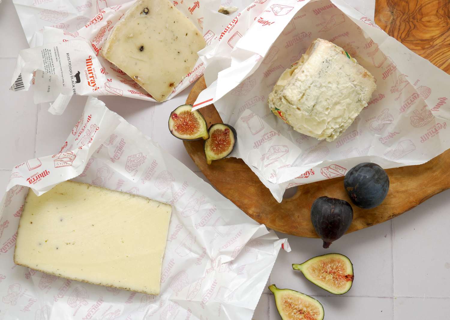 An assortment of cheeses with figs on parchment paper and a wooden serving platter