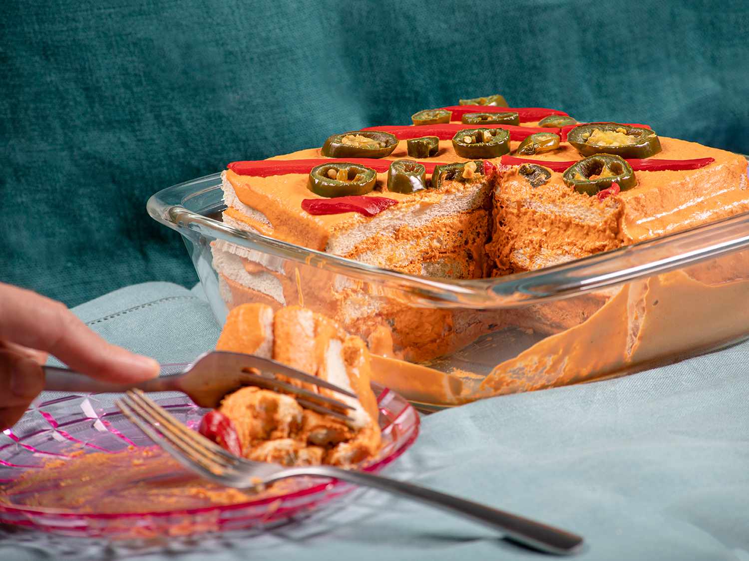 Side view of a pastel de atun with a hand using a fork to eat a cut slice off a festive pink plate