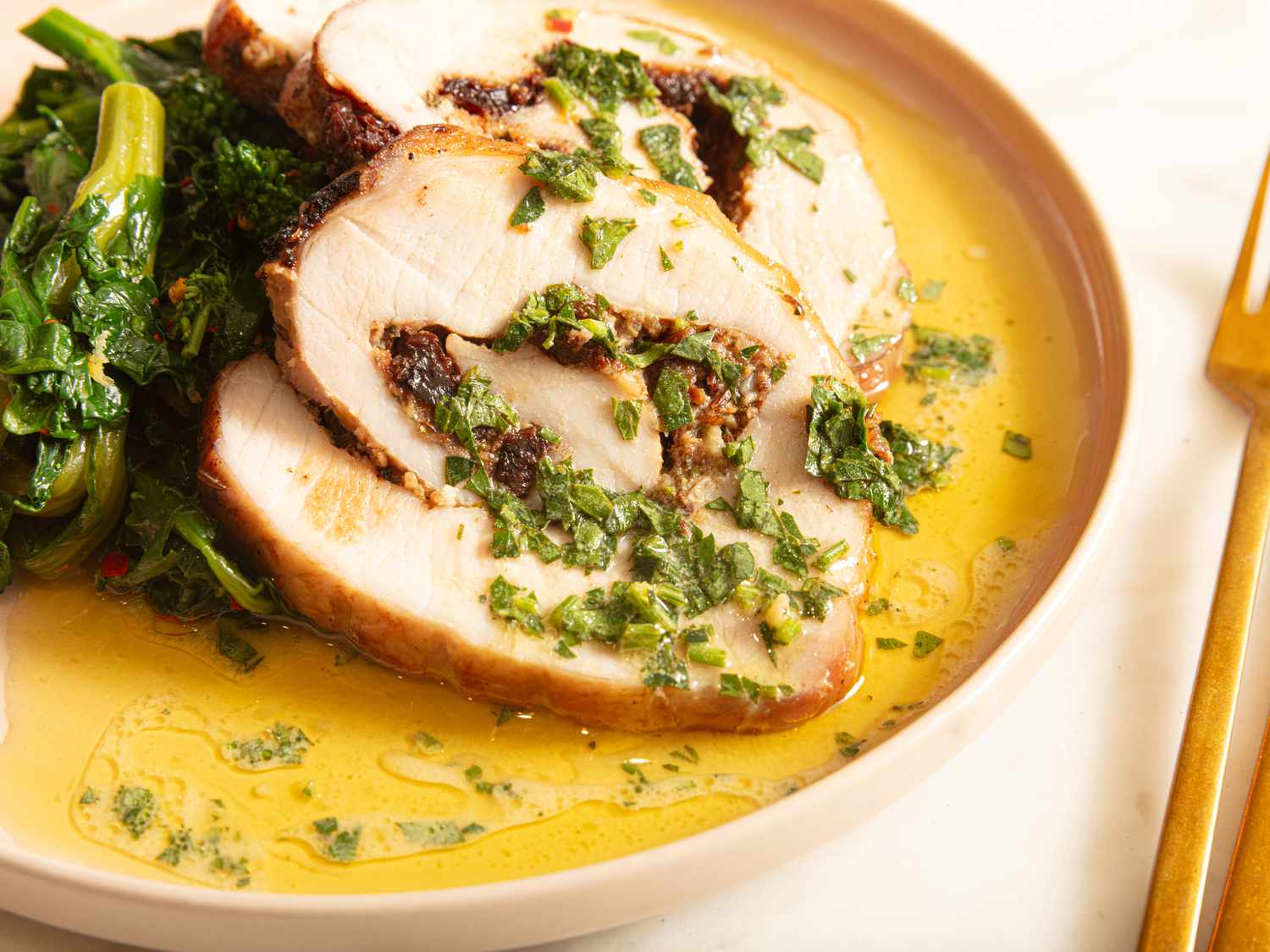 Sliced of pork loin on a dish with sauteed greens and a lemon vinaigrette sauce, with gold fork to the right side 