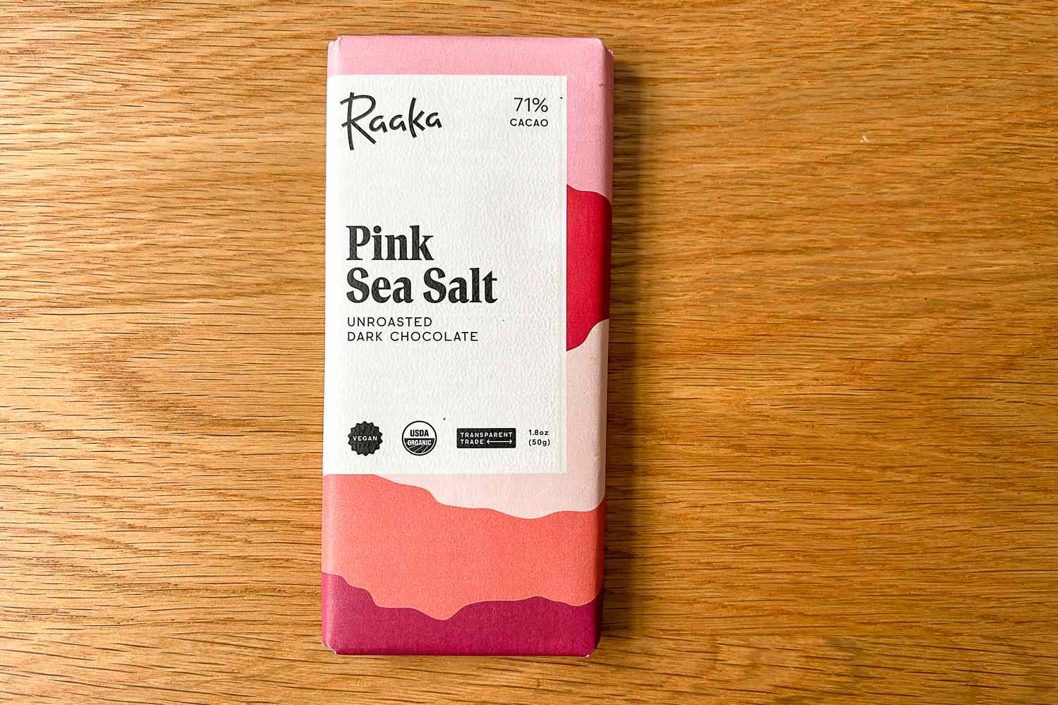 The Raaka Pink Sea Salt Dark Chocolate Bar on a wooden surface