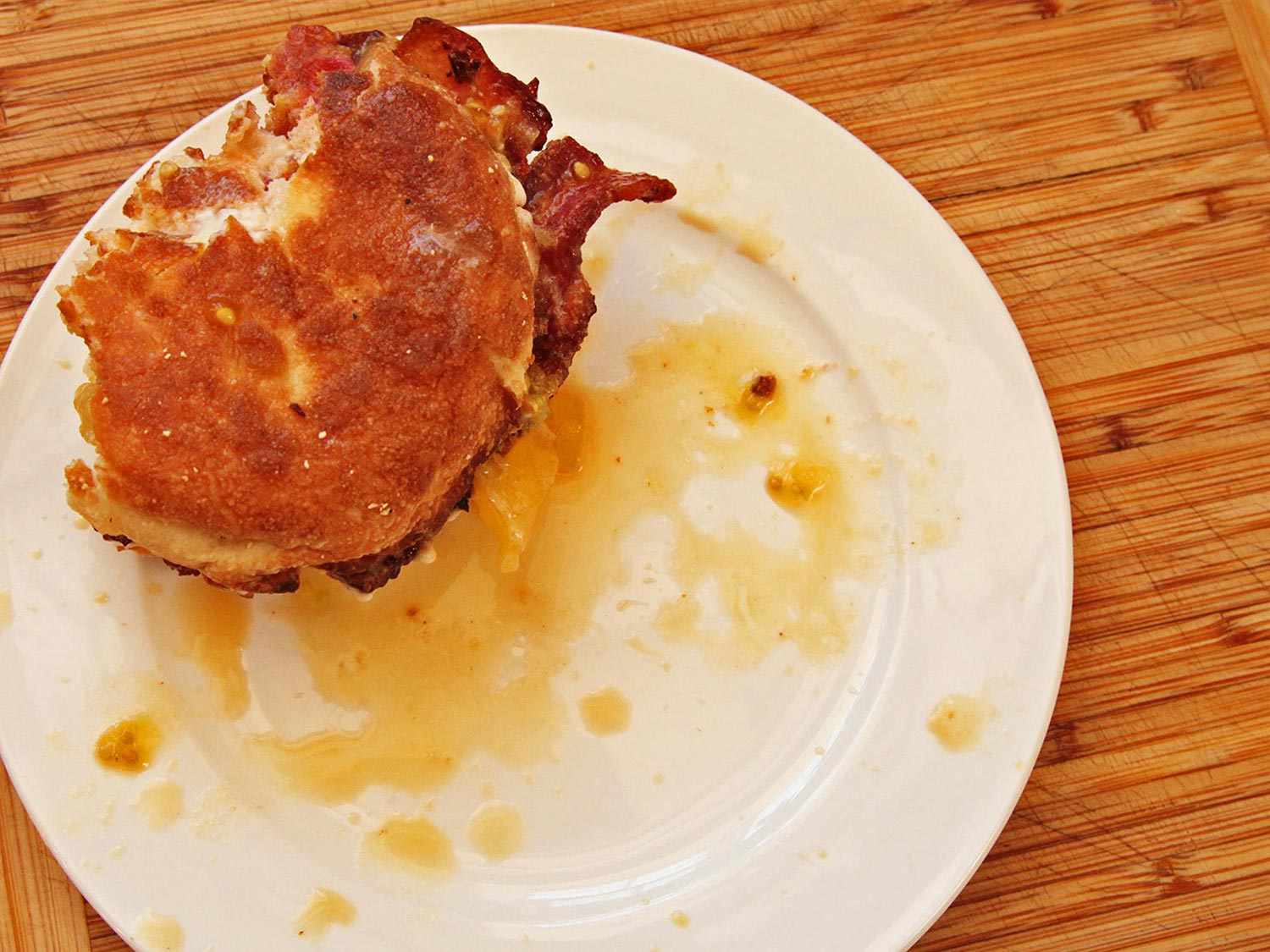 Half-eaten bacon, tomato, and mayo English muffin sandwich on a plate, with grease drippings visible