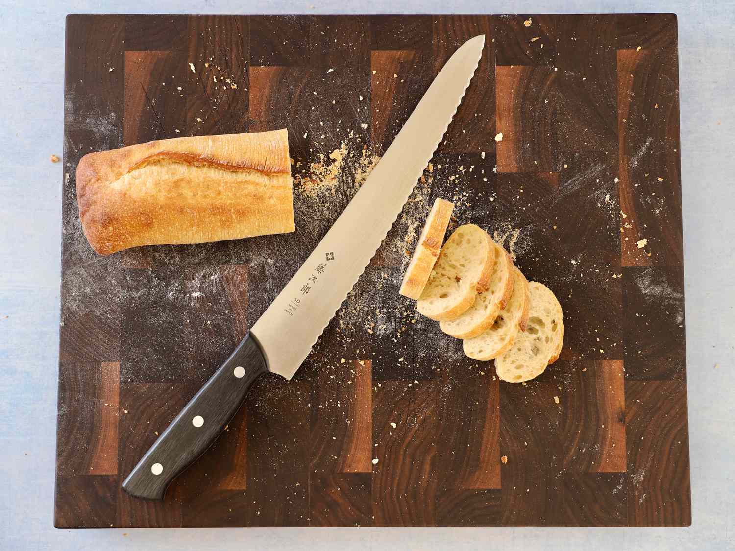 Tojiro Bread Slicer 270mm F-687 displayed on a wood cutting board with a partially sliced baguette