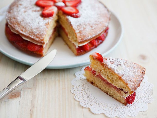 Victoria sponge cake, with a slice cut out and placed on a doily. 