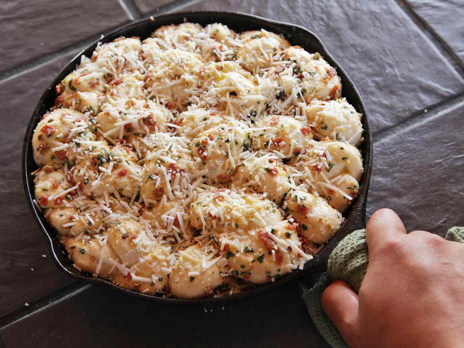 A cast iron pan of cheese-covered pepperoni garlic knots ready to bake