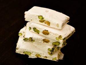 Closeup of torrone, cut into slabs and stacked on a black surface.
