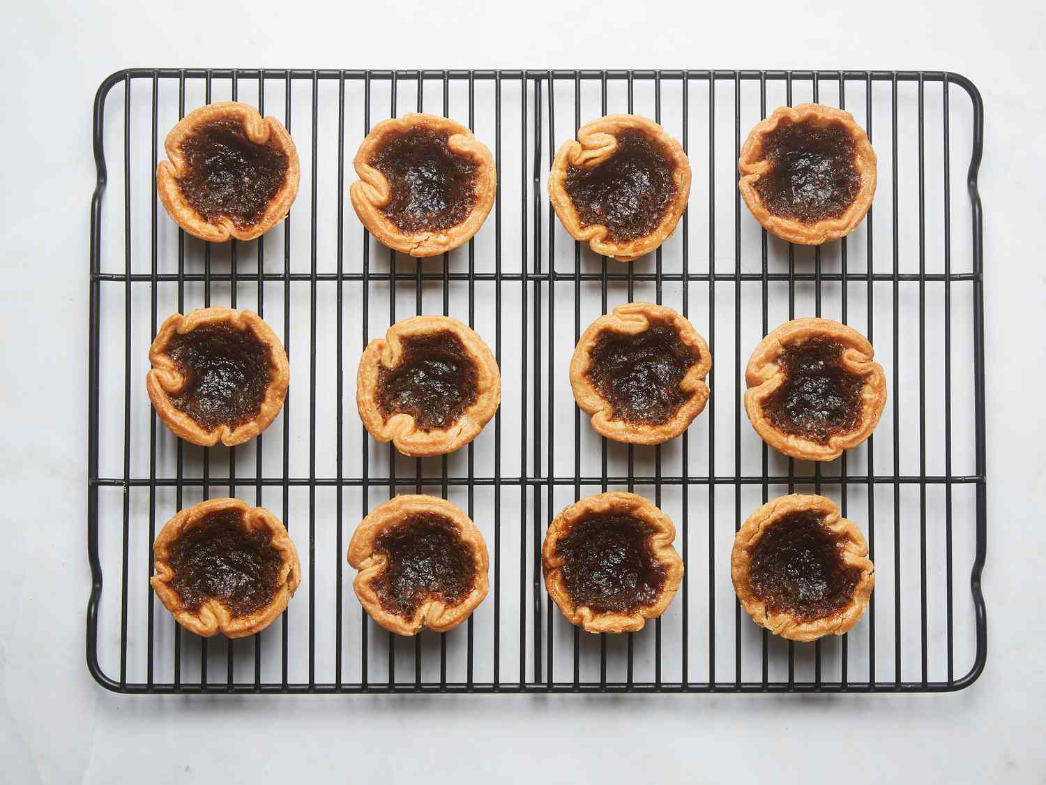 The tarts resting on a cooling rack on a white marble surface 