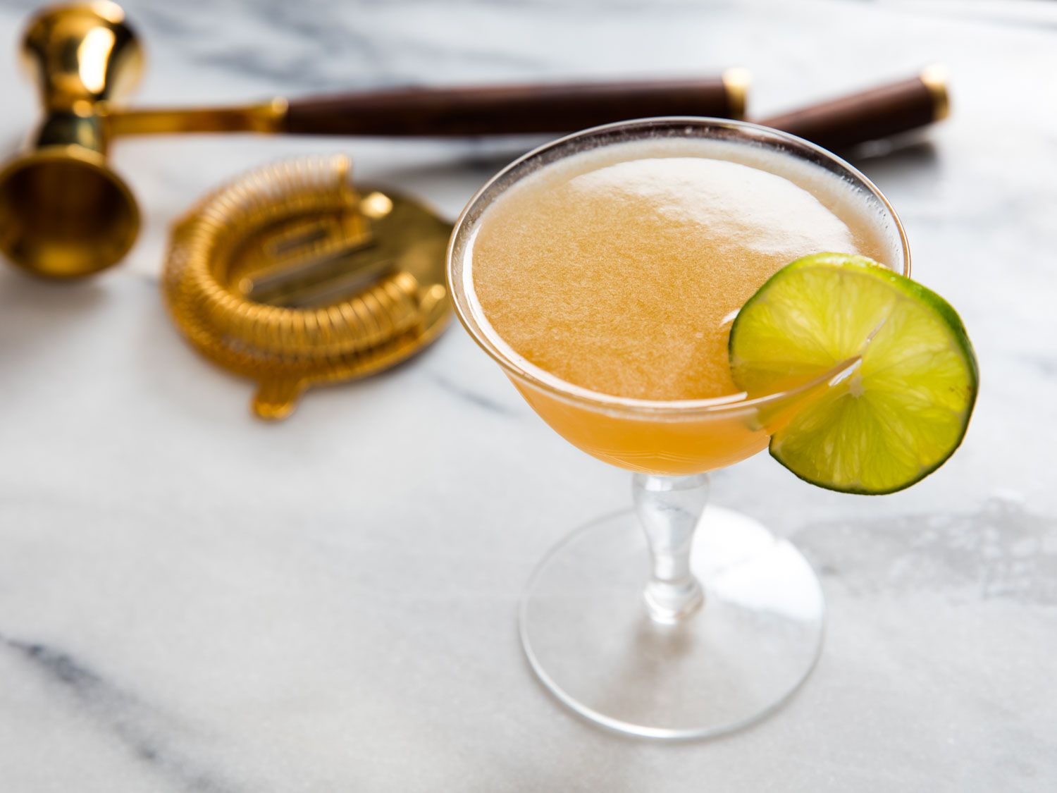 A daiquiri With Scotch and maple served in a cocktail glass with a lime wheel.