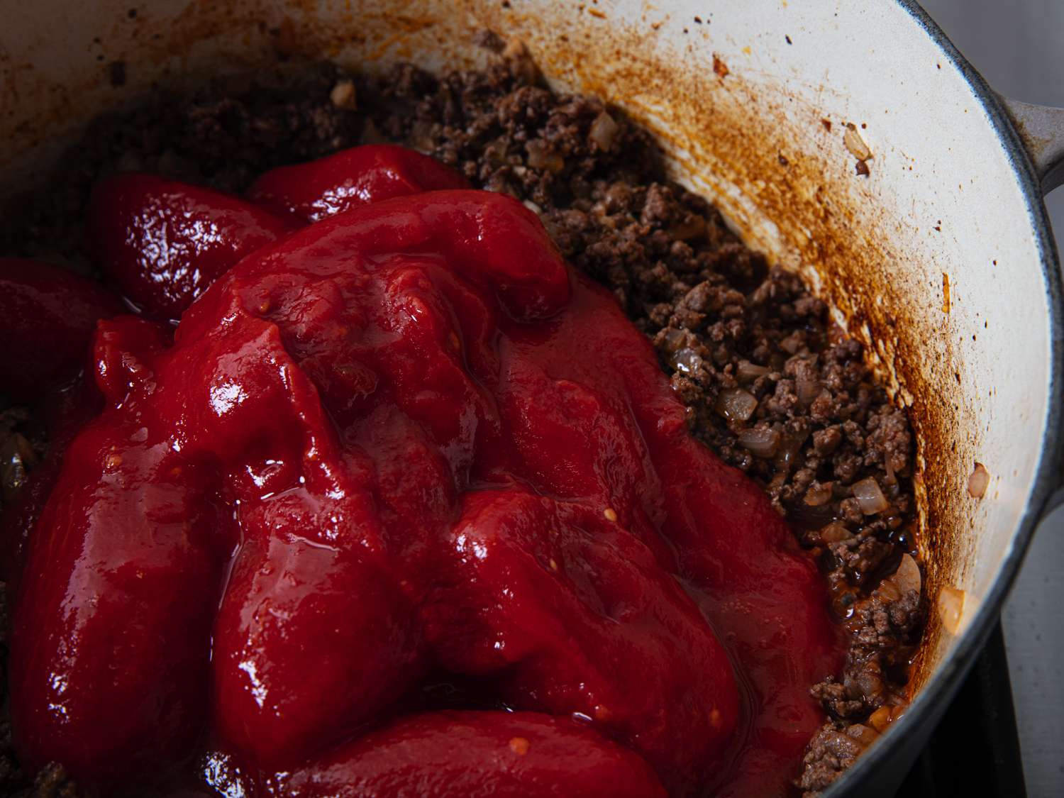 Overhead view of canned tomatoes added to meat in pot