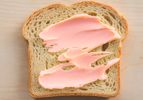 A slice of bread with pink spread on a light surface
