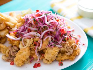 A pile of fried mixed seafood topped with lime-marinated red onions, tomatoes, and cilantro