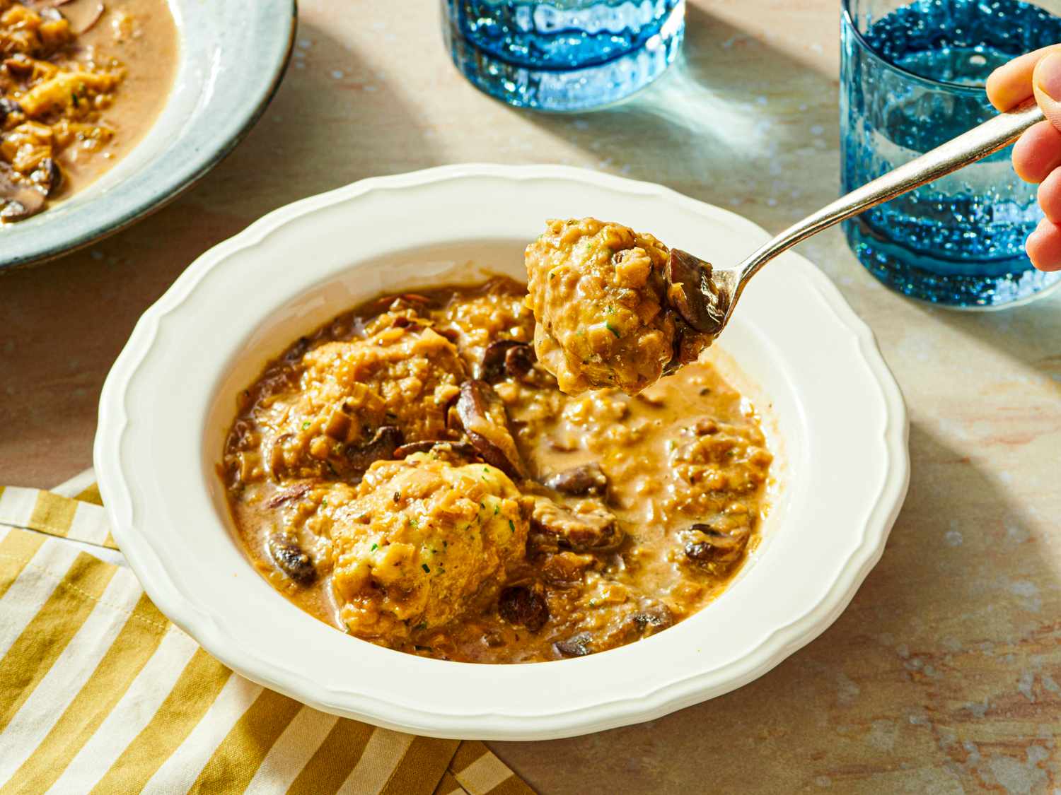 Bowl of soup with mushroom chunks and dumplings spoon lifting a dumpling