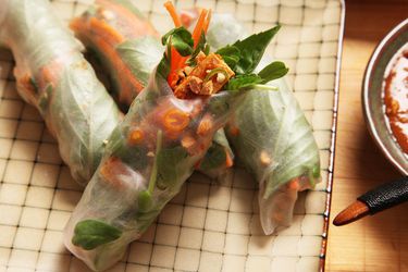 Clsoeup of vegan crispy tofu spring rolls. A ramekin of peanut-tamarind dipping sauce is off to one side.