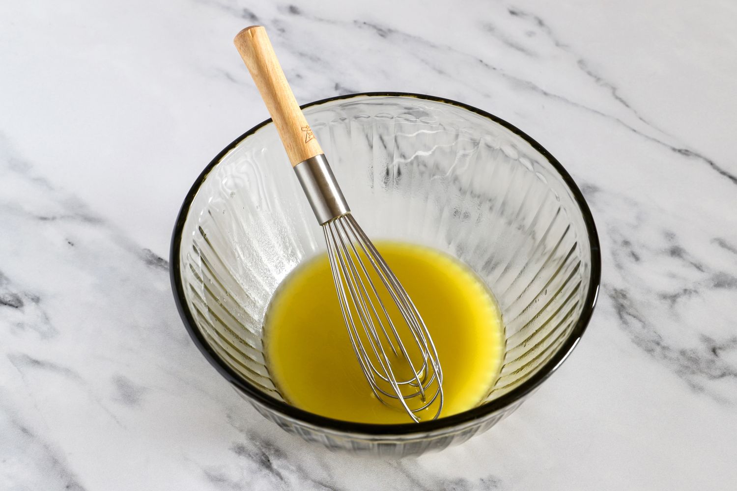 A whisk resting in a Pyrex bowl containing liquid on a marble surface