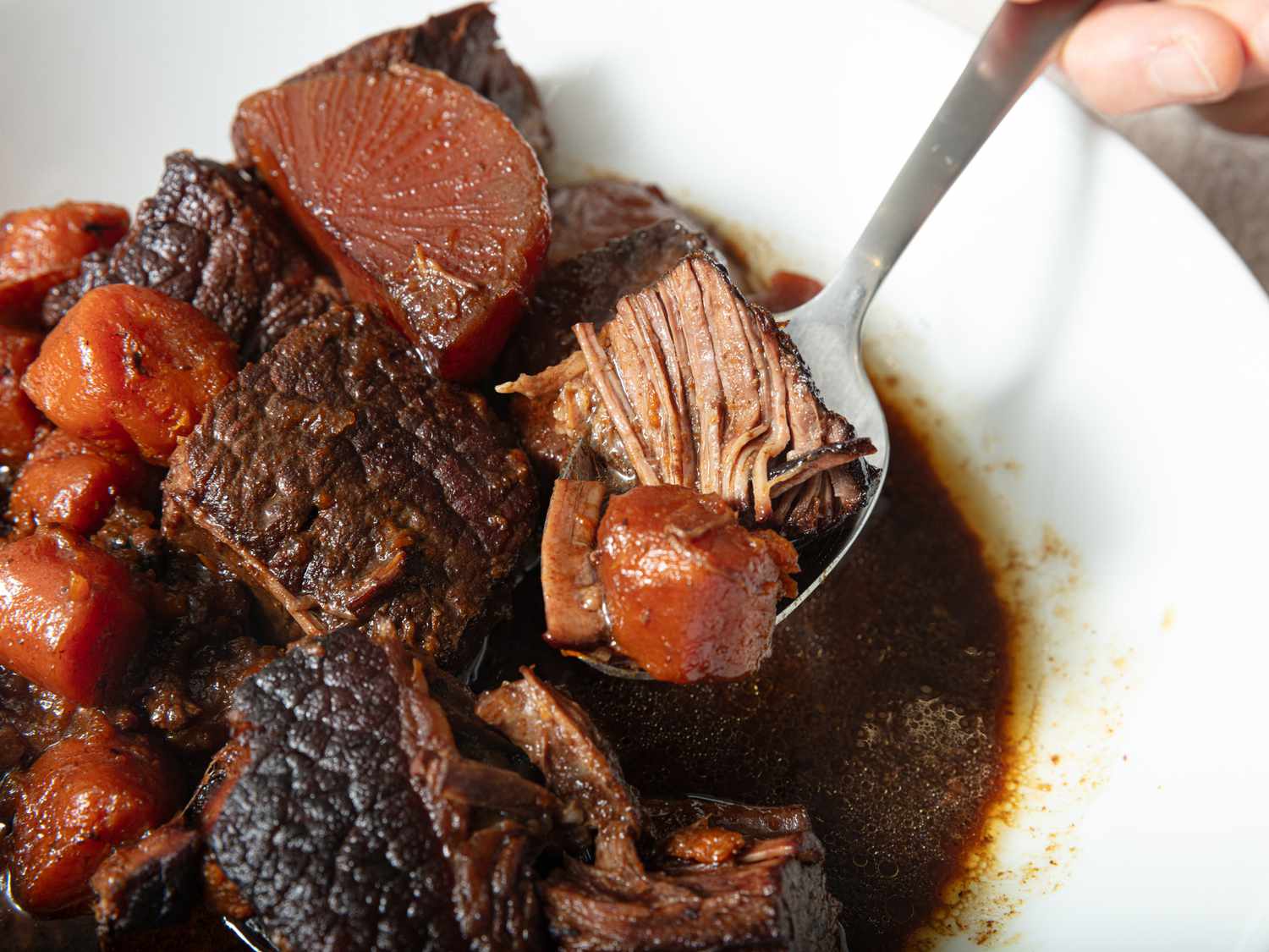 white dish of Cantonese braised brisket with a spoon of beef and daikon on a white tablecloth
