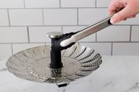 A person lifting the KitchenAid steamer basket with tongs.