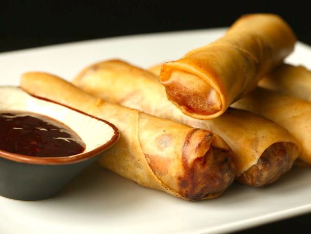 Crispy pork and cabbage egg rolls served on a plate with a ramekin of plum sauce for dipping.