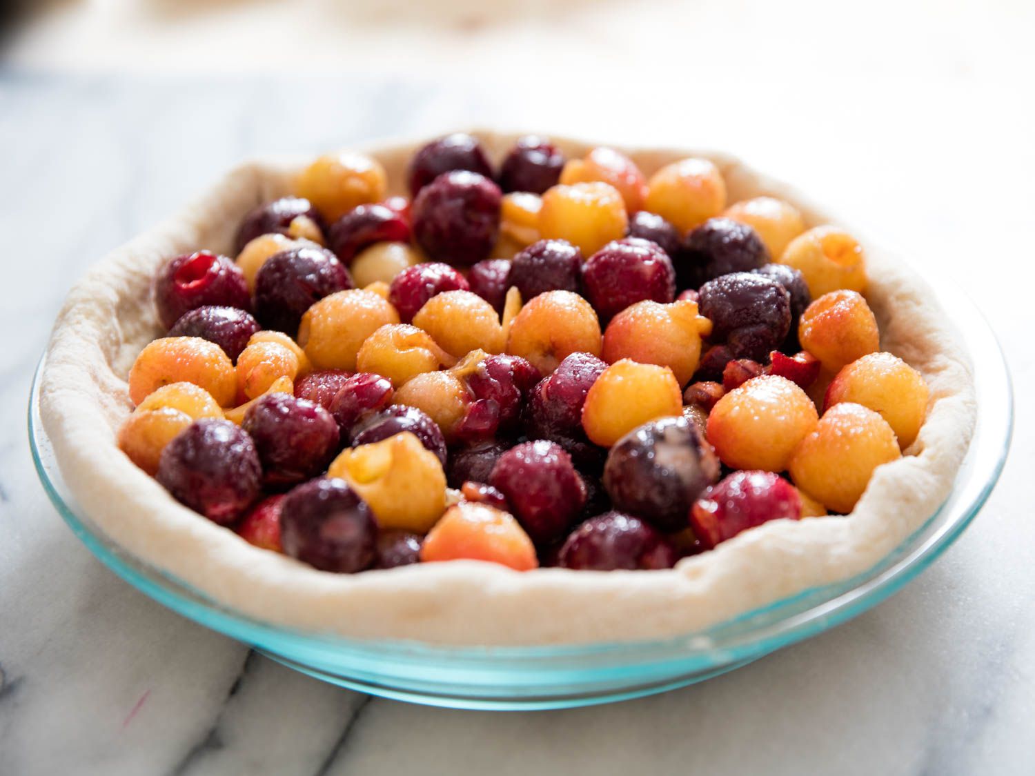 Cherries piled onto a pie crust inside a glass pie dish. 