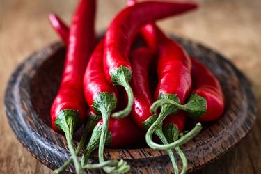 A pile of red chile peppers on a small wood dish. 