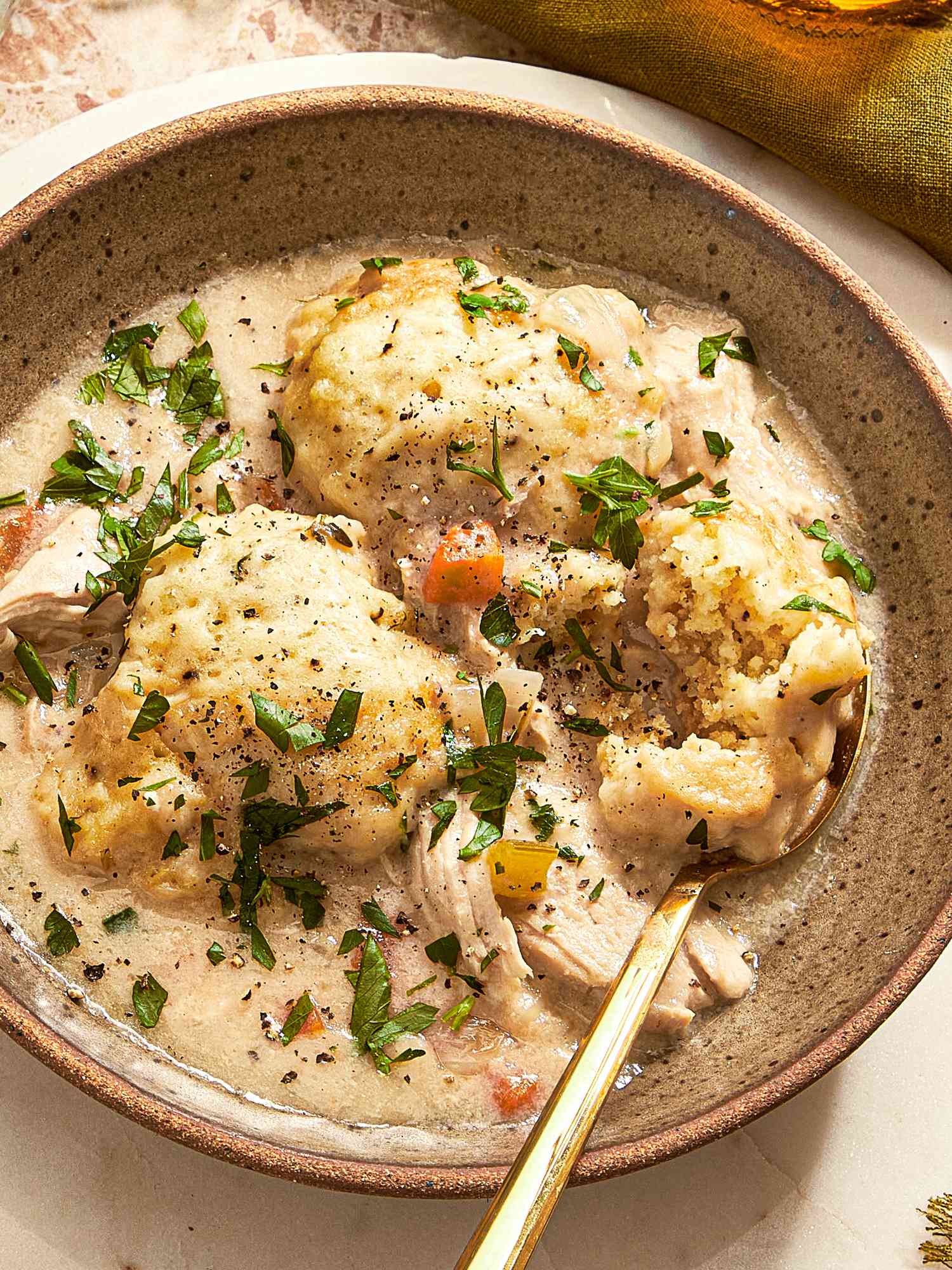 Close up of a bowl of Chicken Dumpling soup in rustic stoneware bowl, with a dark green napkin to the side, and a gold spoon in the soup
