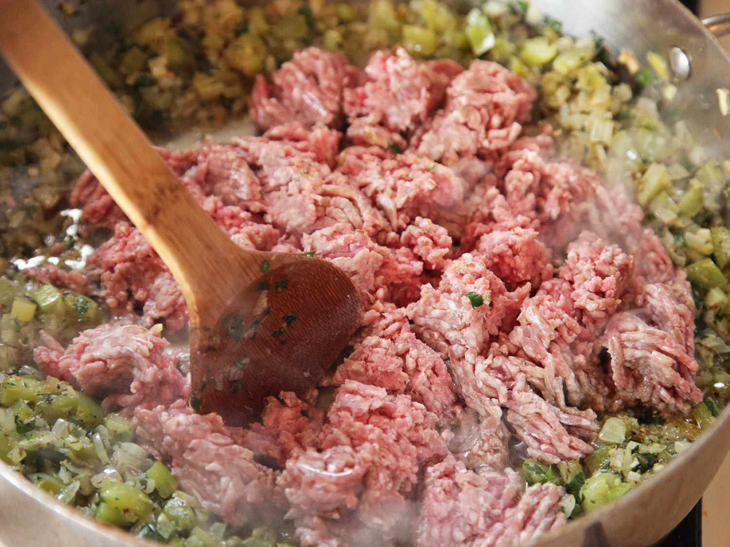 Close-up of a wooden spoon breaking up the ground beef into smaller clumps.