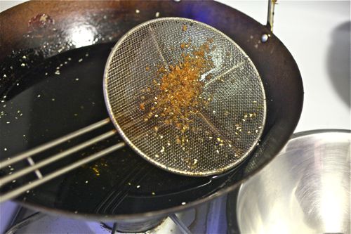 Straining debris from frying oil in wok.