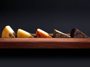 Profile view of five different Manchego-type cheeses, cut into wedges and arranged on a wooden board.