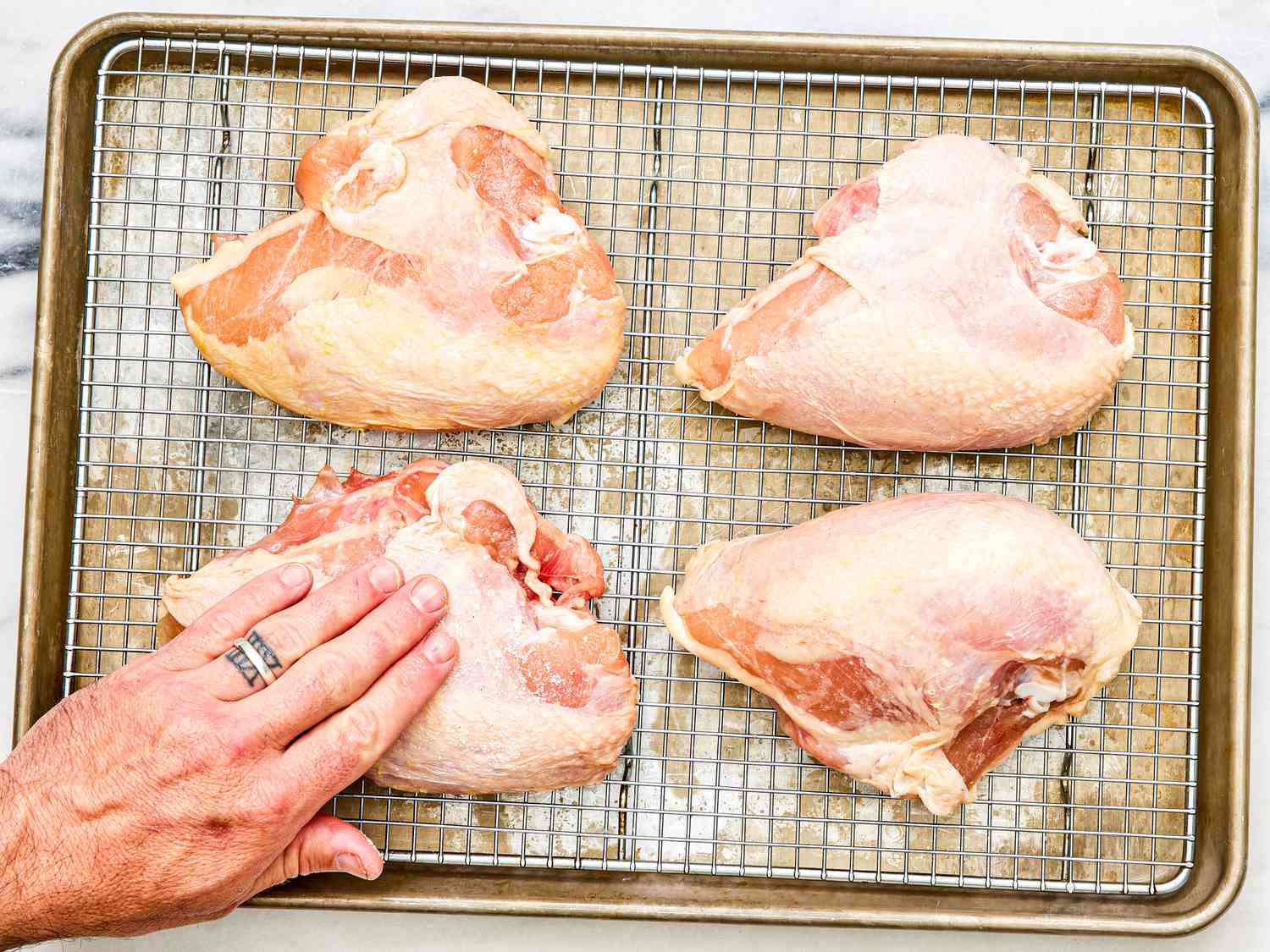 Four bone-in skin-on chicken breasts on a wire rack set in a rimmed baking sheet.