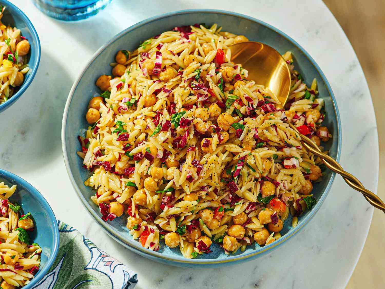 A bowl of orzo pasta salad with chickpeas, garnished with fresh herbs, served with utensils
