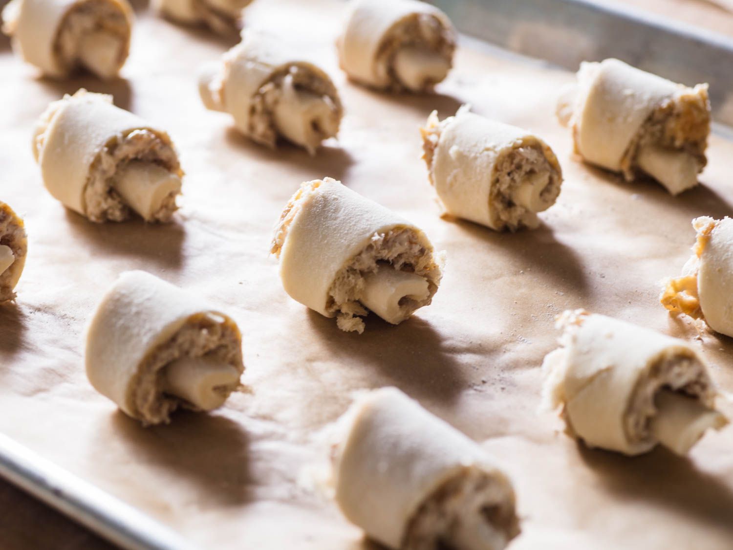 Crescent rugelach evenly spaced on a parchment-lined baking sheet, ready to go in the oven.