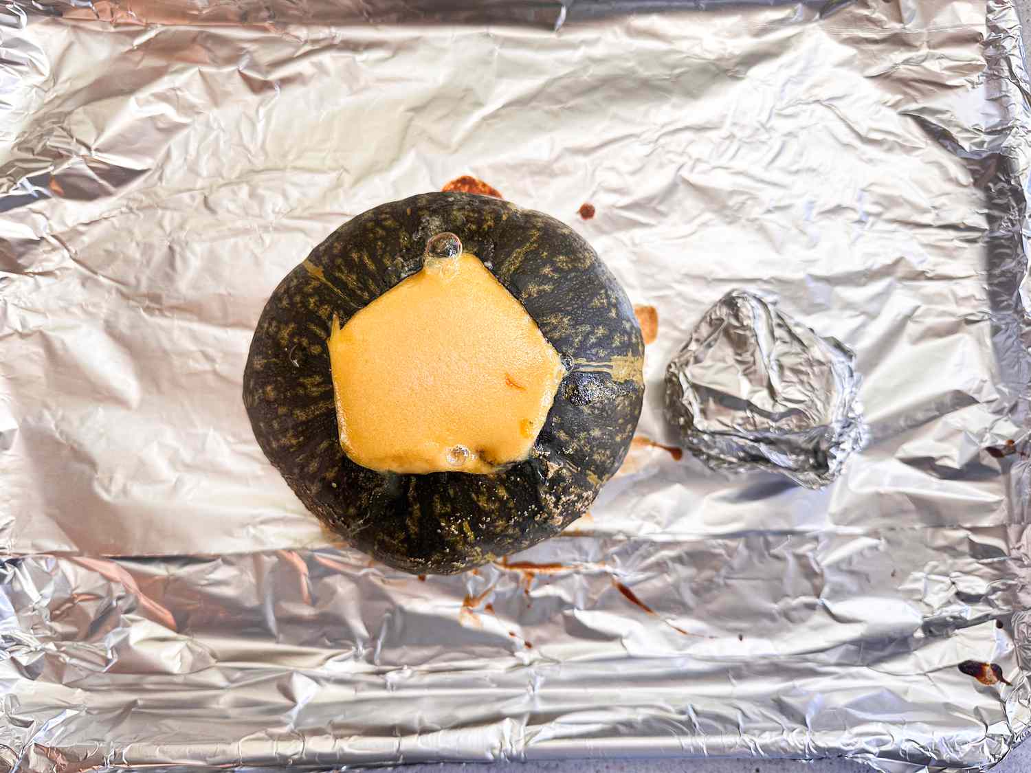 Kobocha after baked, with lid wrapped in foil to the side. Both are on a foil lined baking sheet. 