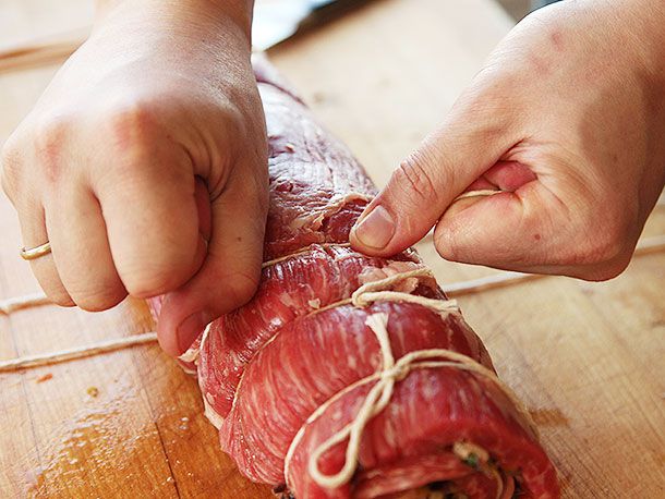 Hands tying butchers twine down length of rolled up flank steak