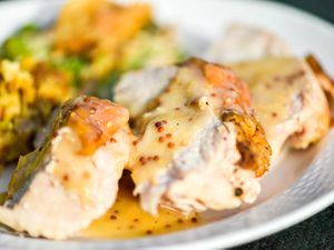 A plate of smoked turkey breast slices with white wine and mustard gravy, all on a white plate with cornbread dressing in the background.. 