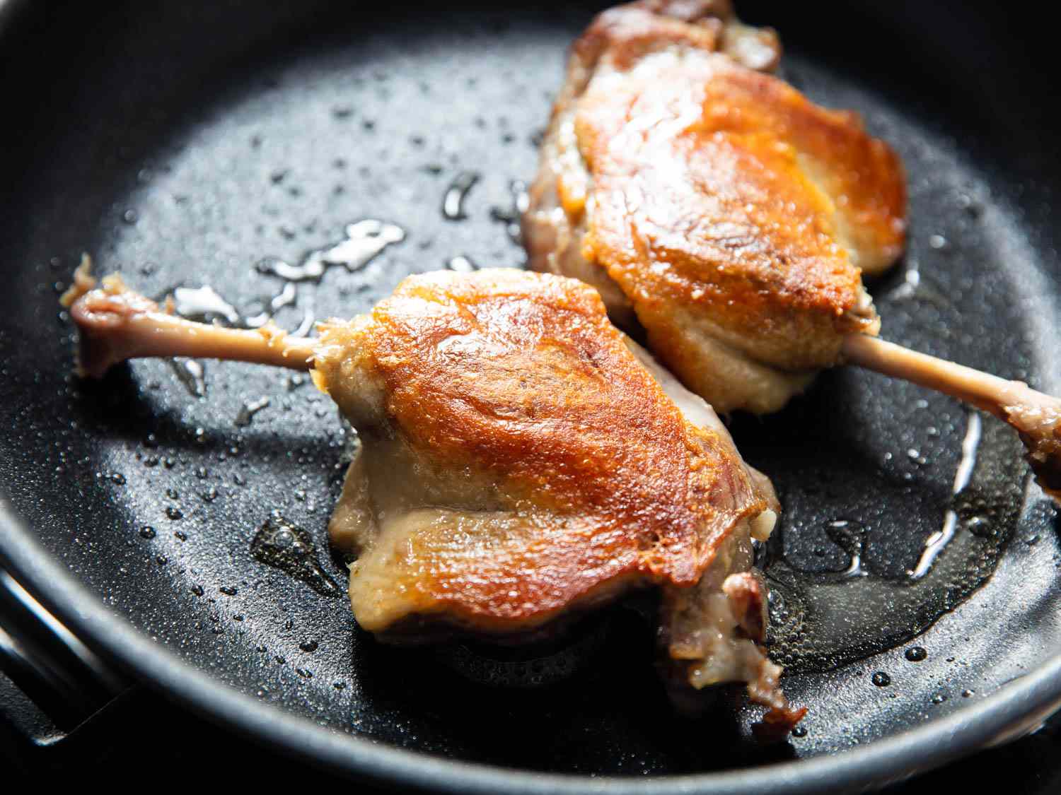 Two duck confit legs in a skillet. 