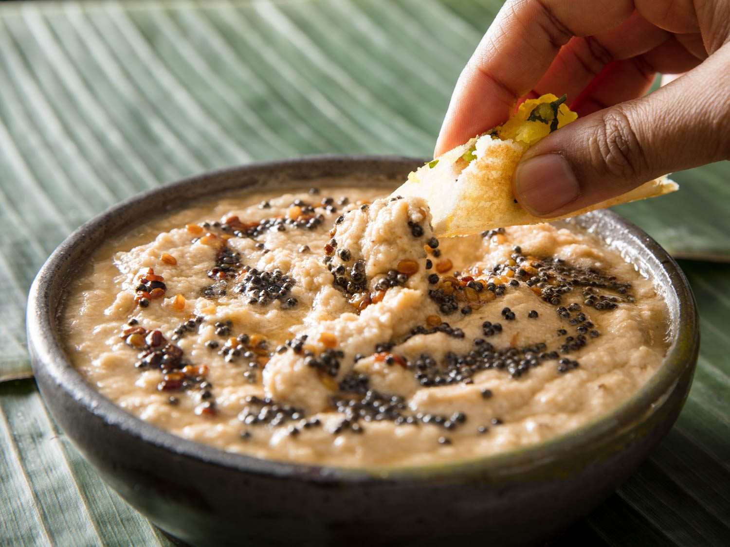 The author's hand dips a piece of dosa into the coconut chutney.