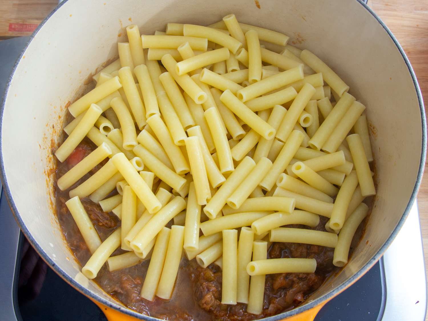 Adding cooked ziti to a pot of Neapolitan beef and onion ragu.